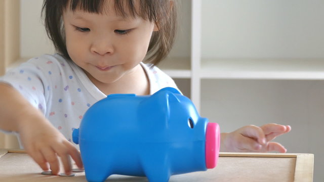 little girl putting money in piggy bank
