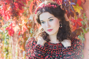 Portrait of fairy autumn girl with red fall wreath at floral background of grape woodbine