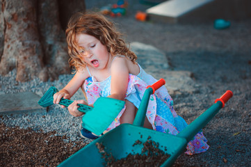 child girl playing with shovel and wheelbarrow on playground