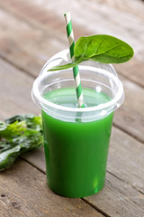 Plastic cup of spinach juice on wooden background