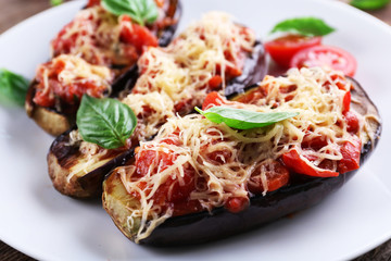 Dish of eggplant with cherry tomatoes and cheese in white plate on wooden table, closeup