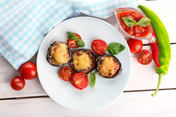 Dish of eggplant with cherry tomatoes and cheese in white plate on wooden table, top view
