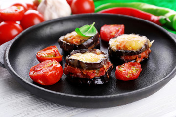 Dish of eggplant with cherry tomatoes and cheese in black pan on wooden table, closeup