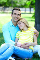 Young pregnant woman with husband sitting on green grass in park