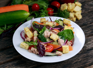 Tuna salad with Spinach, rocket, red ruby chard, tomatoes, cucumbers, carrot, red onion, croutons on old wooden table