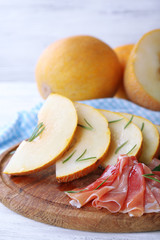 Melon with prosciutto of Parma ham on wooden table, closeup