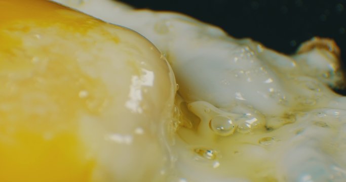 Extreme macro of greasy fried egg on frying pan. 4K