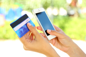 Cellphone and credit card in woman's hands outdoors, close up