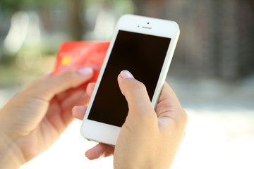 Cellphone and credit card in woman's hands outdoors, close up
