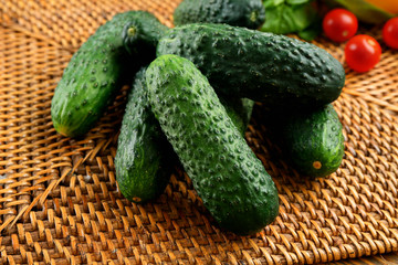 Composition of cucumbers, tomatoes and sweet peppers on wicker serviette against wooden background, close up