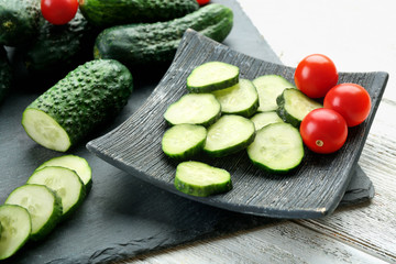 Sliced cucumbers with tomatoes on black plank on wooden background