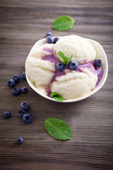 Vanilla ice-cream in a bowl decorated with mint, berries and blueberries syrup on wooden background