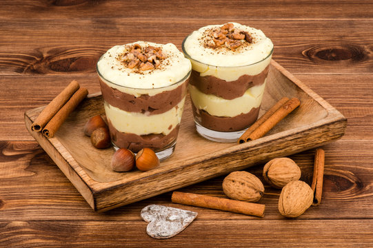 Sweet Dessert - Chocolate And Vanilla Pudding In Glasses Served On The Wooden Tray With Nuts And  Cinnamon Sticks.