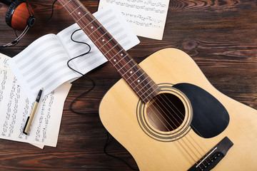 Fototapeta na wymiar Guitar with earphones and music sheets on wooden background