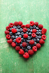 Fototapeta na wymiar Heart shaped raspberries and blueberries on old wooden background