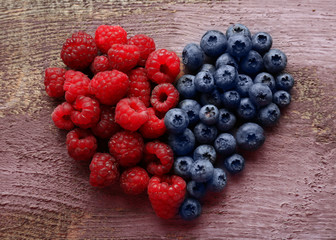 Heart shaped raspberries and blueberries on old wooden background