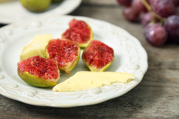 Ripe figs and cheese on plate, on wooden background