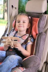 Cute little girl sitting in the car and playing with wooden plane