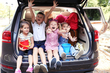 Happy children sit on a car trunk and laughing
