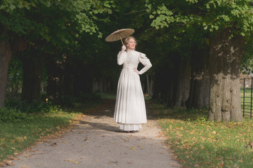 Chique victorian womanwith umbrella walking on path in garden.