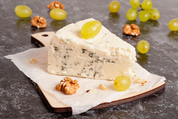 Blue cheese with grapes and nuts on wooden cutting board