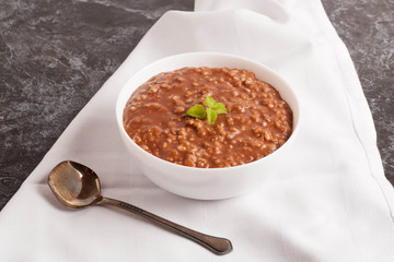 Chocolate porridge with banana in white bowl, decorated mint