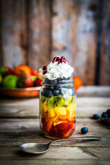 Colorful fruit salad in a jar on rustic wooden background
