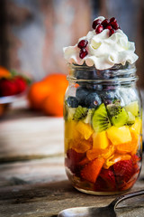 Colorful fruit salad in a jar on rustic wooden background