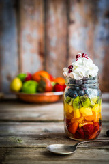 Colorful fruit salad in a jar on rustic wooden background