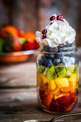Colorful fruit salad in a jar on rustic wooden background
