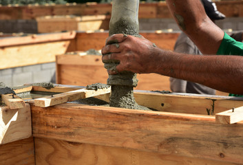 Pouring wet cement to create a tie beam for a concrete block wall is a team effort, and action packed.
