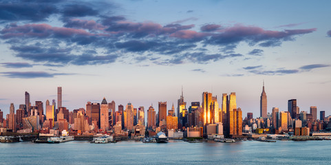 New York City skyline across the Hudson River. The Midtown Manhattan skyscrapers reflect the sunset light