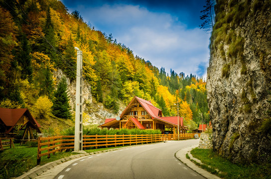 Fall colors around a cottage house. Autumn landscape in mountains with colorful forest and blue sky.