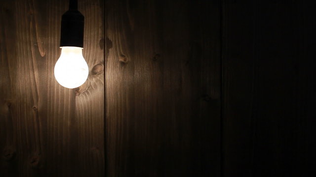Lightbulb switched on and off in front of grungy wooden wall