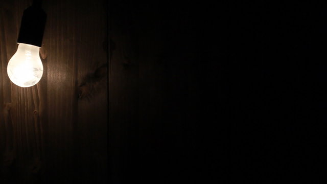 Lightbulb swinging in front of wooden wall