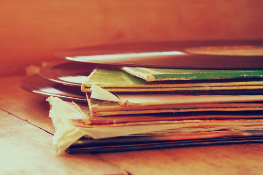 selective focus of records stack with record on top over wooden table. vintage filtered
