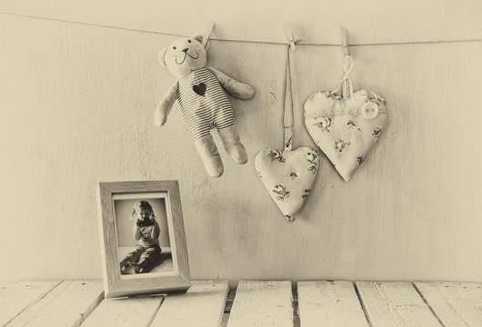 teddy bear over wood table next to photo frame with kid's old photography and fabric hearts. retro filtered image. old style photo
