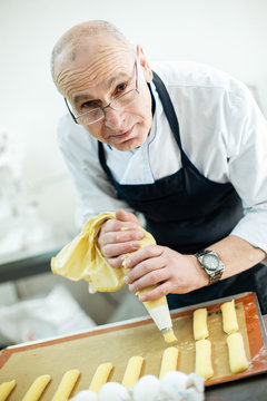Baker prepares a cake and eclairs