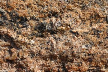 Broken stone grainy surface close-up. Yellow-orange pattern with black and transparent inclusions.