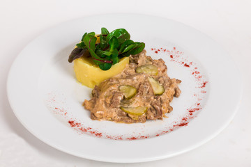 beef goulash stroganoff with pickles and mashed potatoes on a plate isolated white background close-up