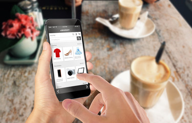 Smart phone online shopping in man hand. Desk with caffe in background. Buy clothes shoes...