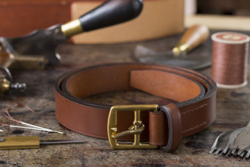 Leather goods craftsman's tools and a ready belt on a dirty work bench