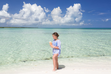 beautiful charming stylish  little girl walking along the beach and tranquil inviting ocean , holding bread in her hands and feeding the fish