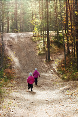 Two little girls running in a beautiful sunny autumn forest