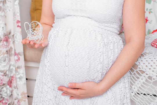 Pregnant woman in a white dress holding self for stomach and small stroller