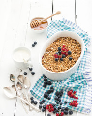 Healthy breakfast. Oat granola berry crumble with fresh blueberries, yogurt and honey in ceramic baking dish over white rustic backdrop