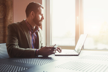 bearded man working with laptop and phone in morning sunlight