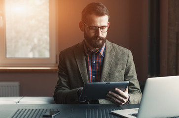 bearded man working with laptop and digital tablet in morning 
