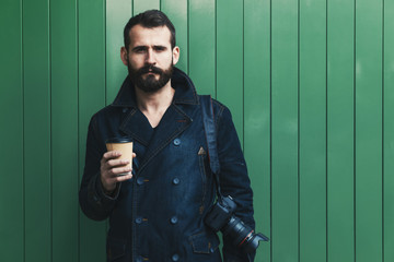 bearded man with paper coffee cup and camera on green wall 