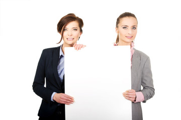 Two businesswomen carrying a big white board.